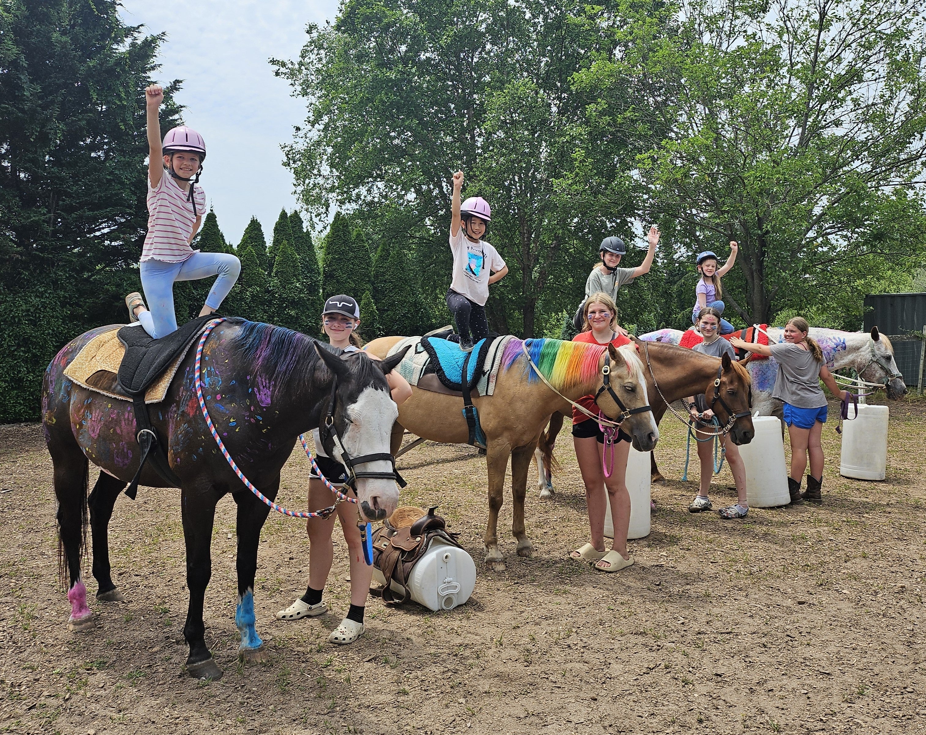 A group of children posing with horses that are decorated with multicolored patterns. The children appear to be smiling and enjoying the experience.