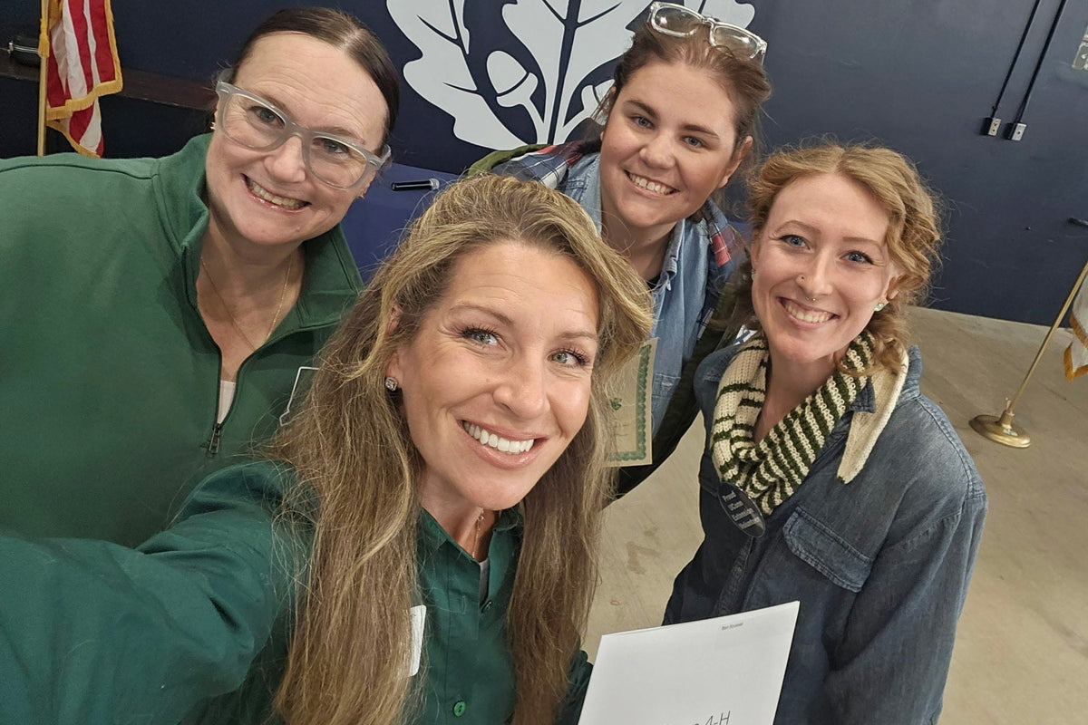 Four women posing for a selfie with a blue wall and American flag in the background